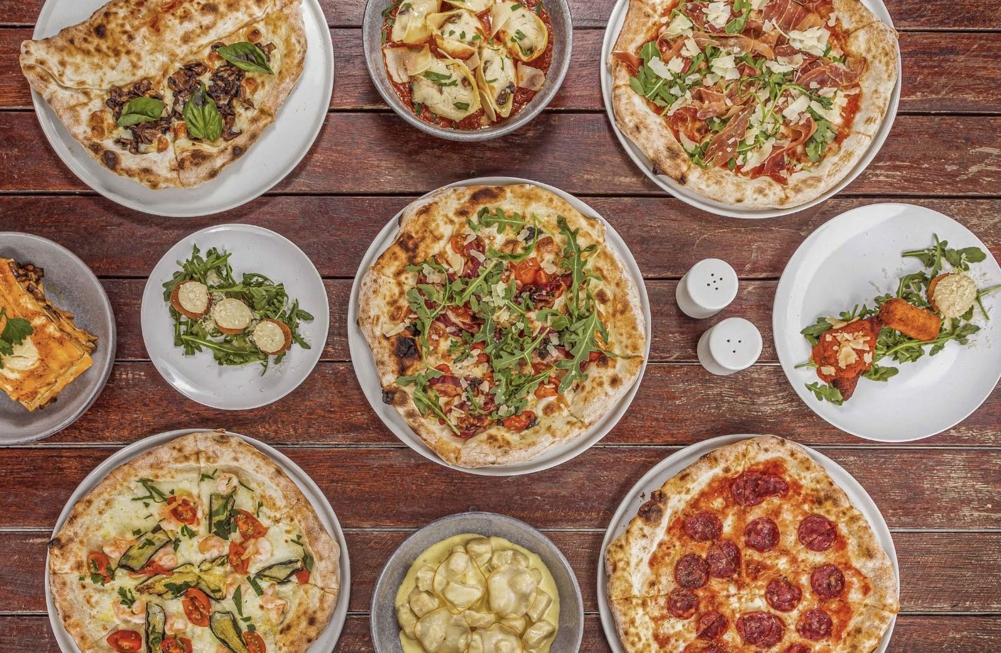 Pizzas, pasta and salads from The Pizza Garden on a wooden table